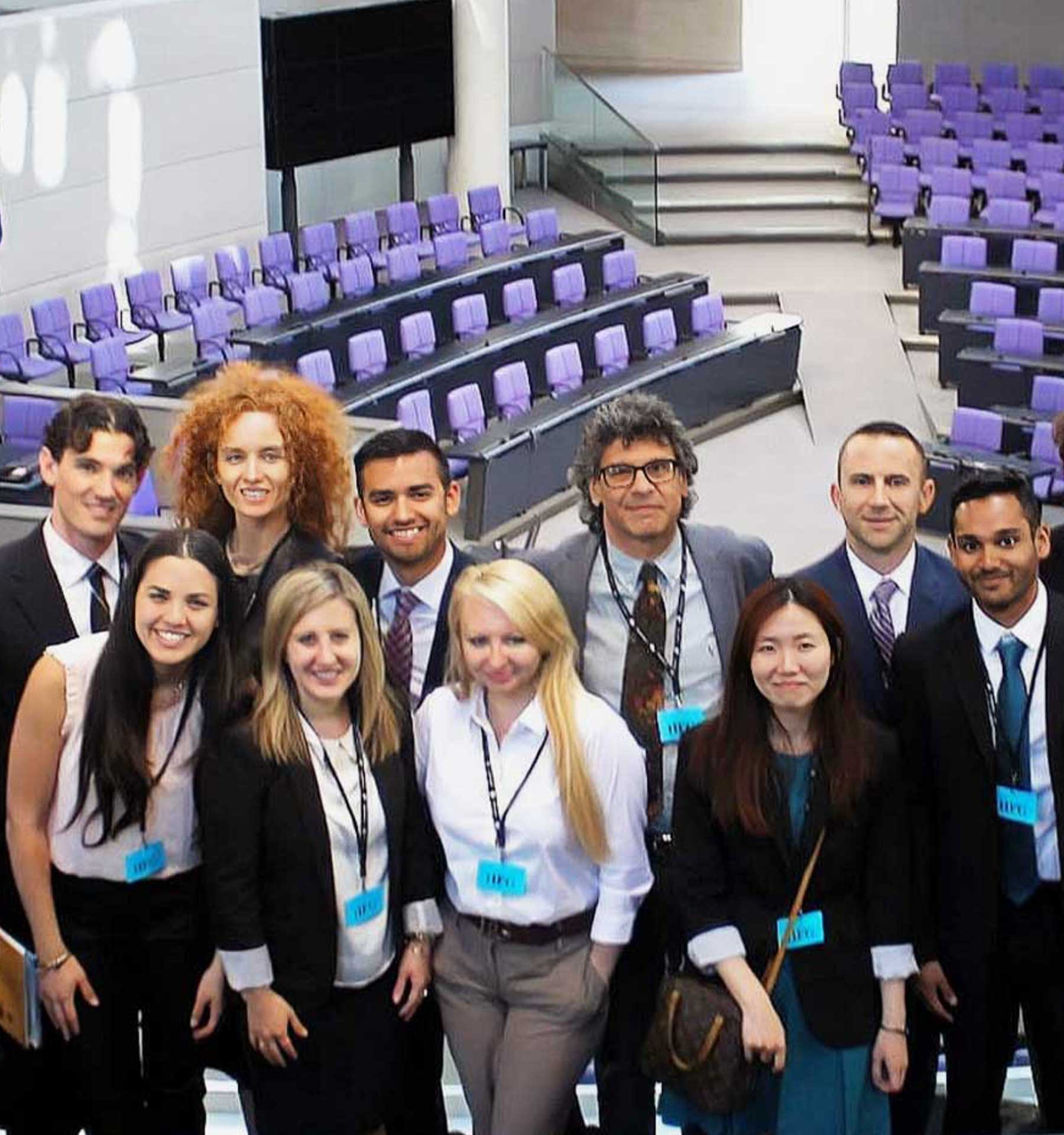 A diverse group of people stands in a brightly lit room, smiling for a photo in front of Canadian, UN, and U.S. flags.