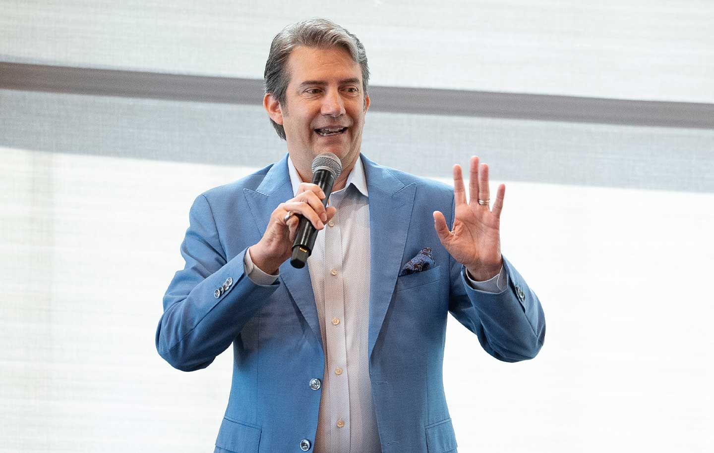 Person speaking with a microphone, wearing a light blue suit on stage.