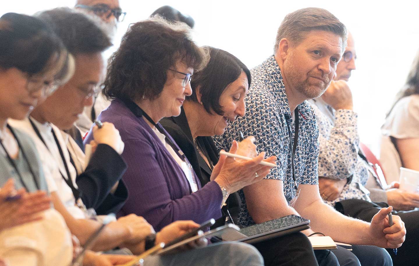 A group of diverse people seated, engaged in a discussion or meeting, in a bright room.