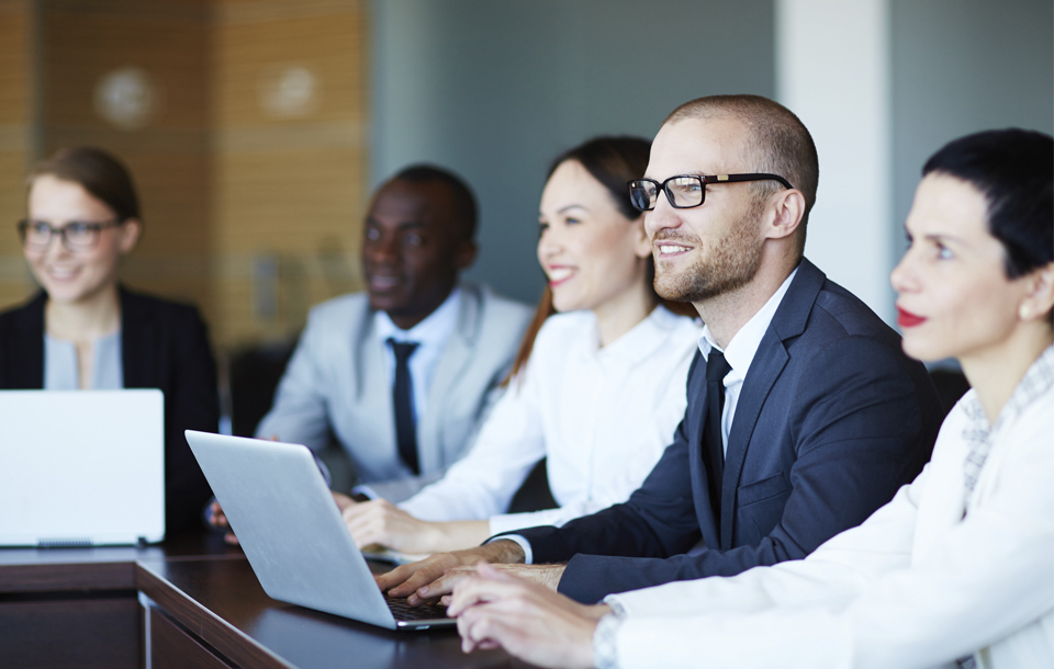 Professionals sit at a table reviewing laptops