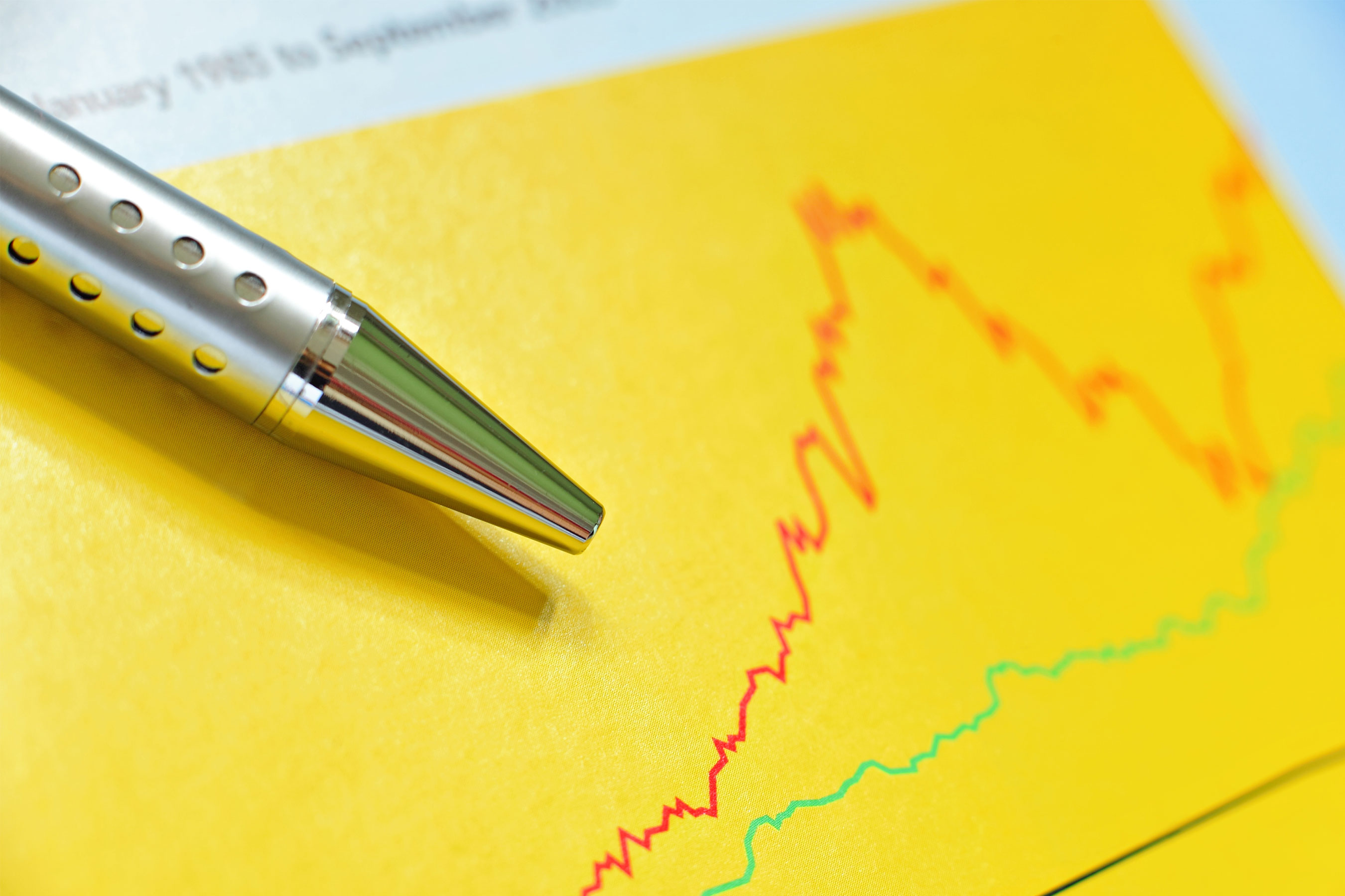 Silver pen on top of yellow financial chart.