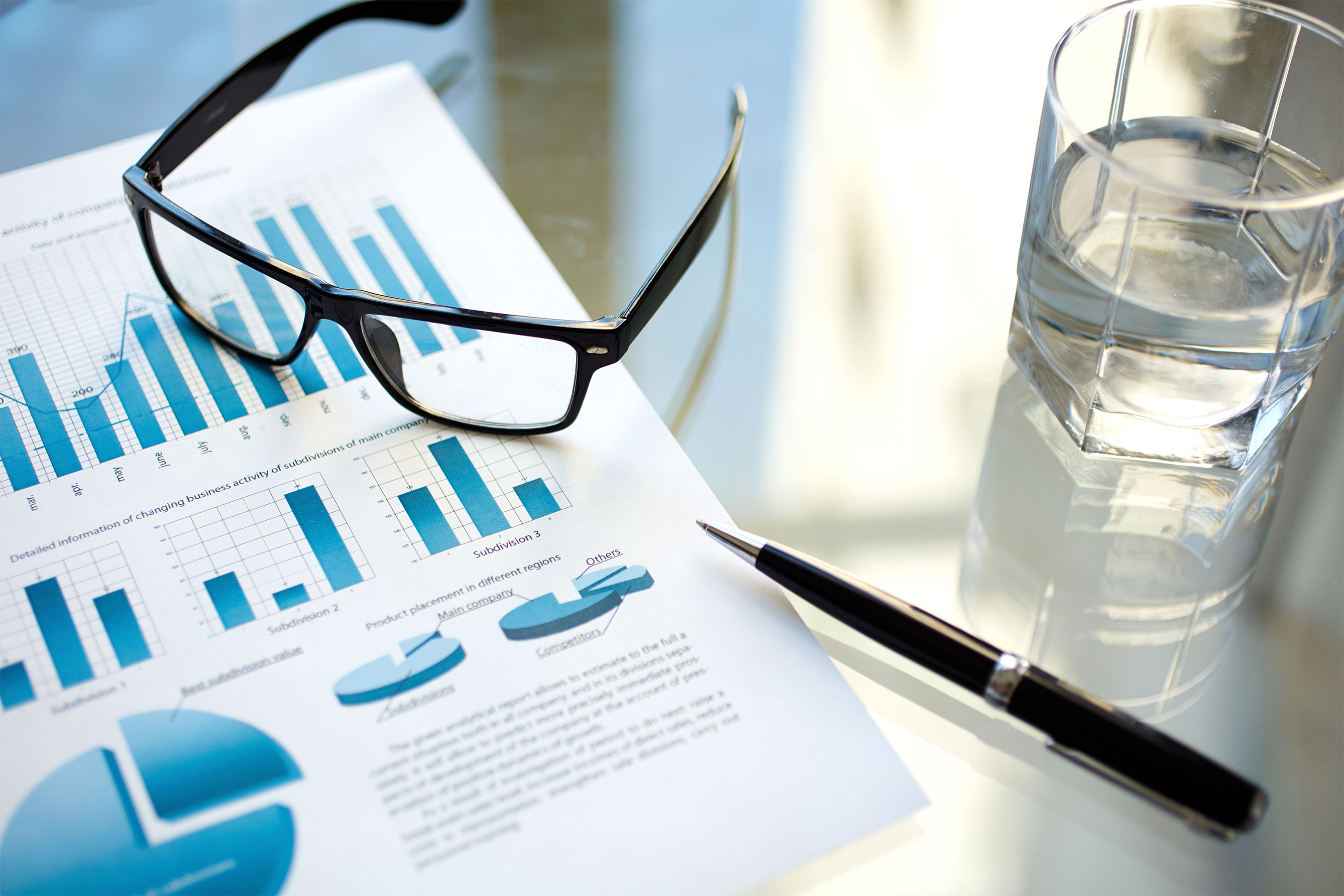 Product management charts, glasses, a black pen, and a glass of water on a table.