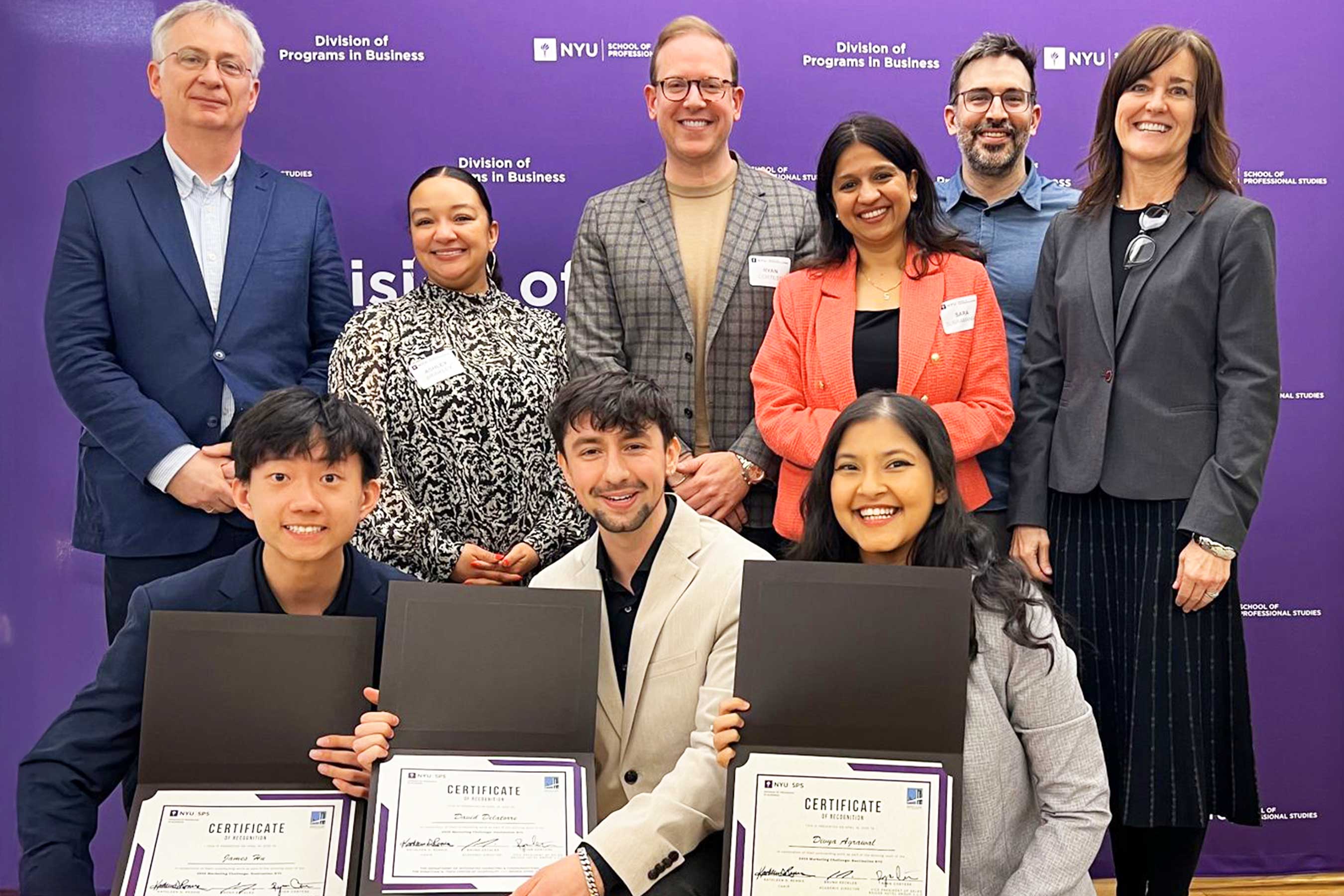 Group of people holding certificates in front of an NYU backdrop.