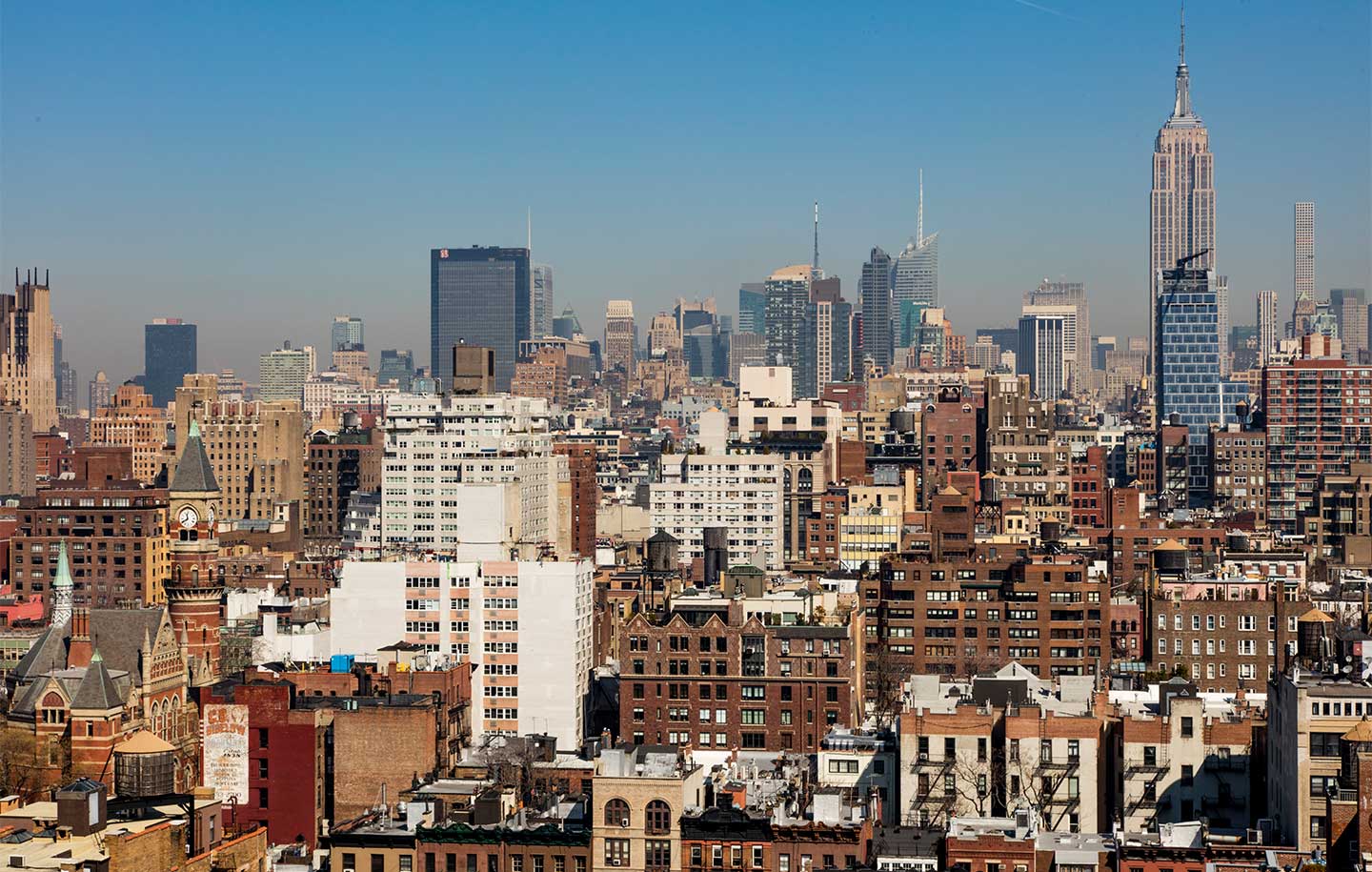 Panoramic view of New York City skyline under a clear blue sky, featuring a mix of historic and modern skyscrapers, evoking a sense of urban vibrancy.