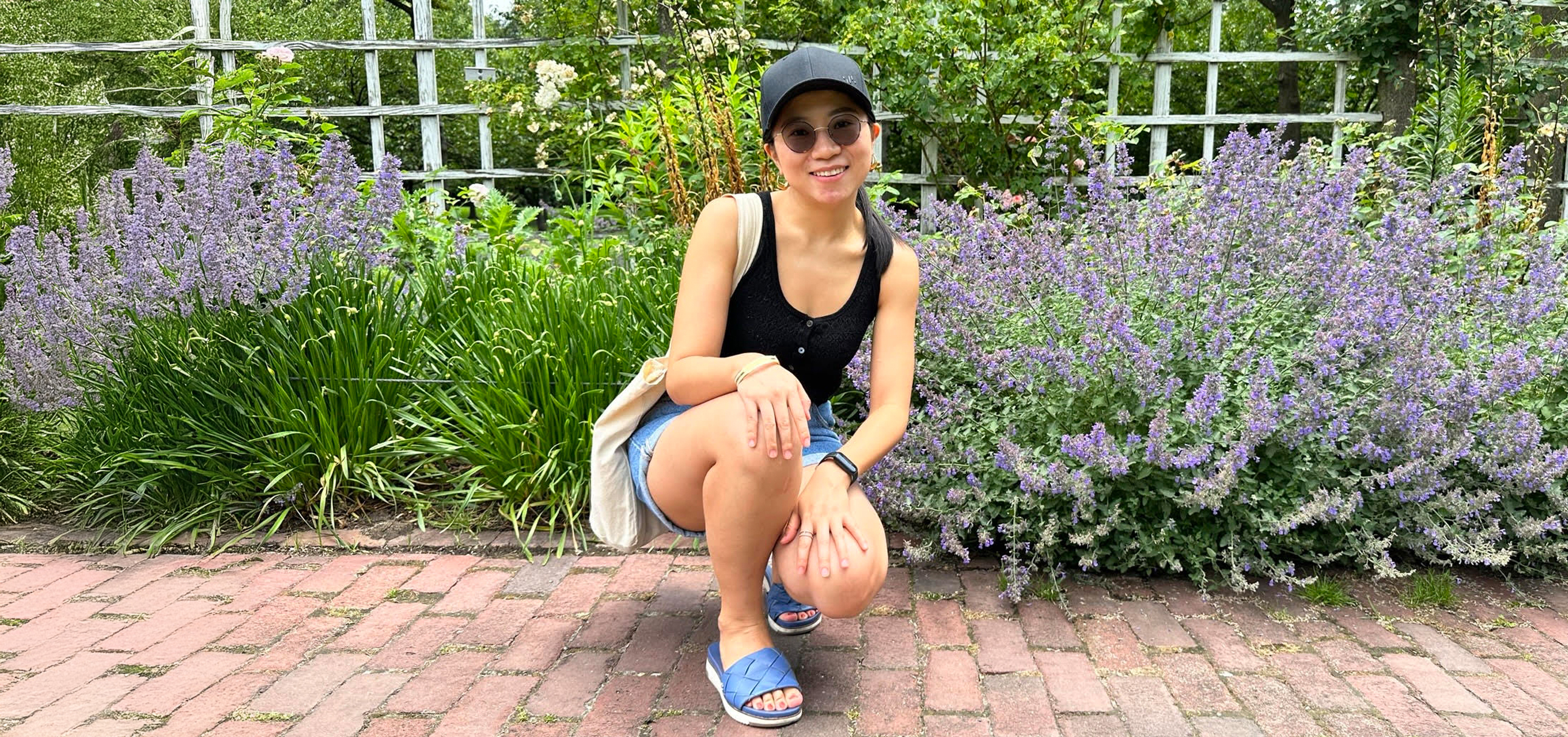 Anny Wangyu, Division of Programs in Business at NYU SPS student, poses for a photo in front of a bush full of purple flowers.
