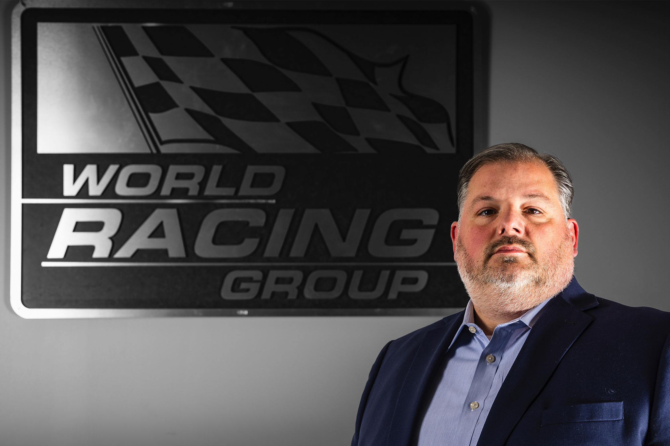 NYU SPS CE faculty member Charles Mellilo poses for a photo in front of a World Racing Group sign