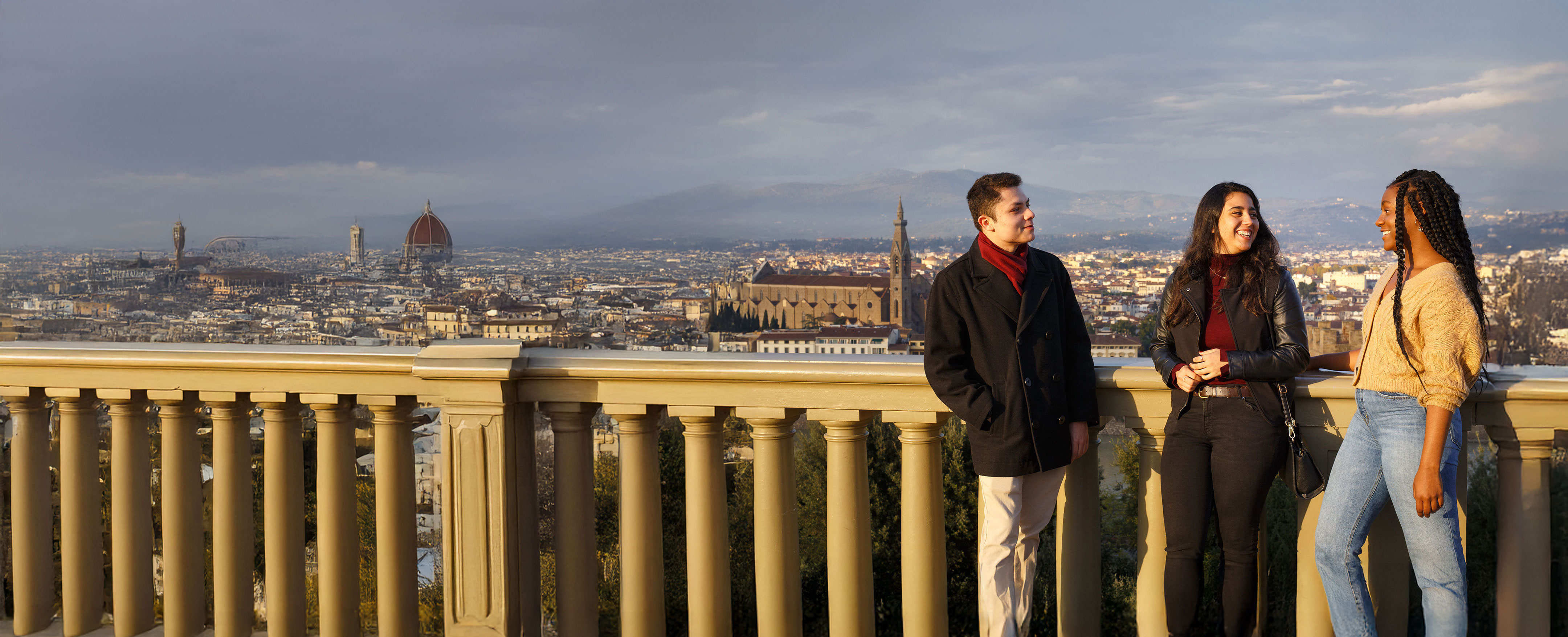 Three NYU students talk on a balcony overlooking a city.